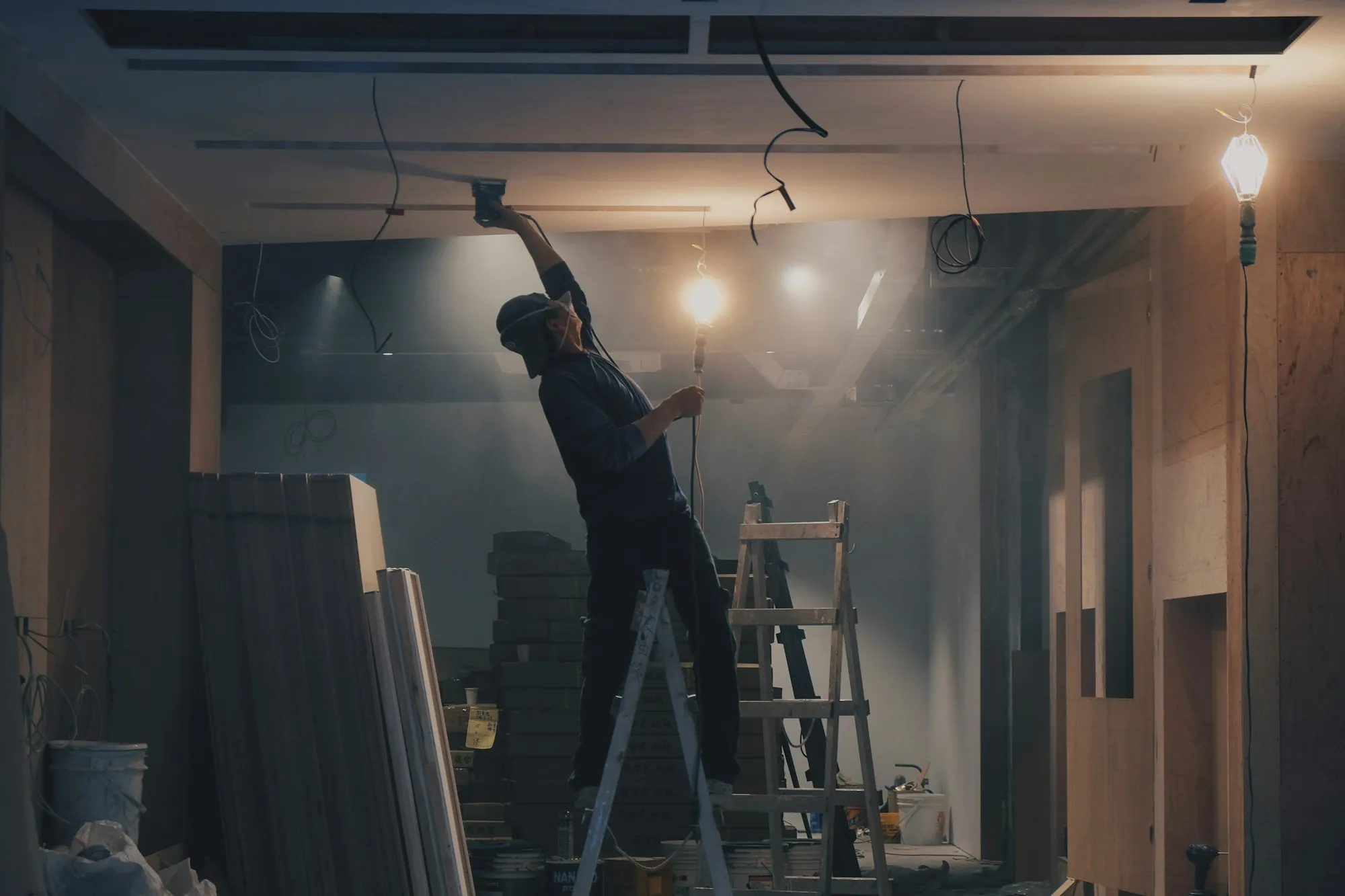 Worker on a stepladder fitting a ceiling fixture in a room under renovation
