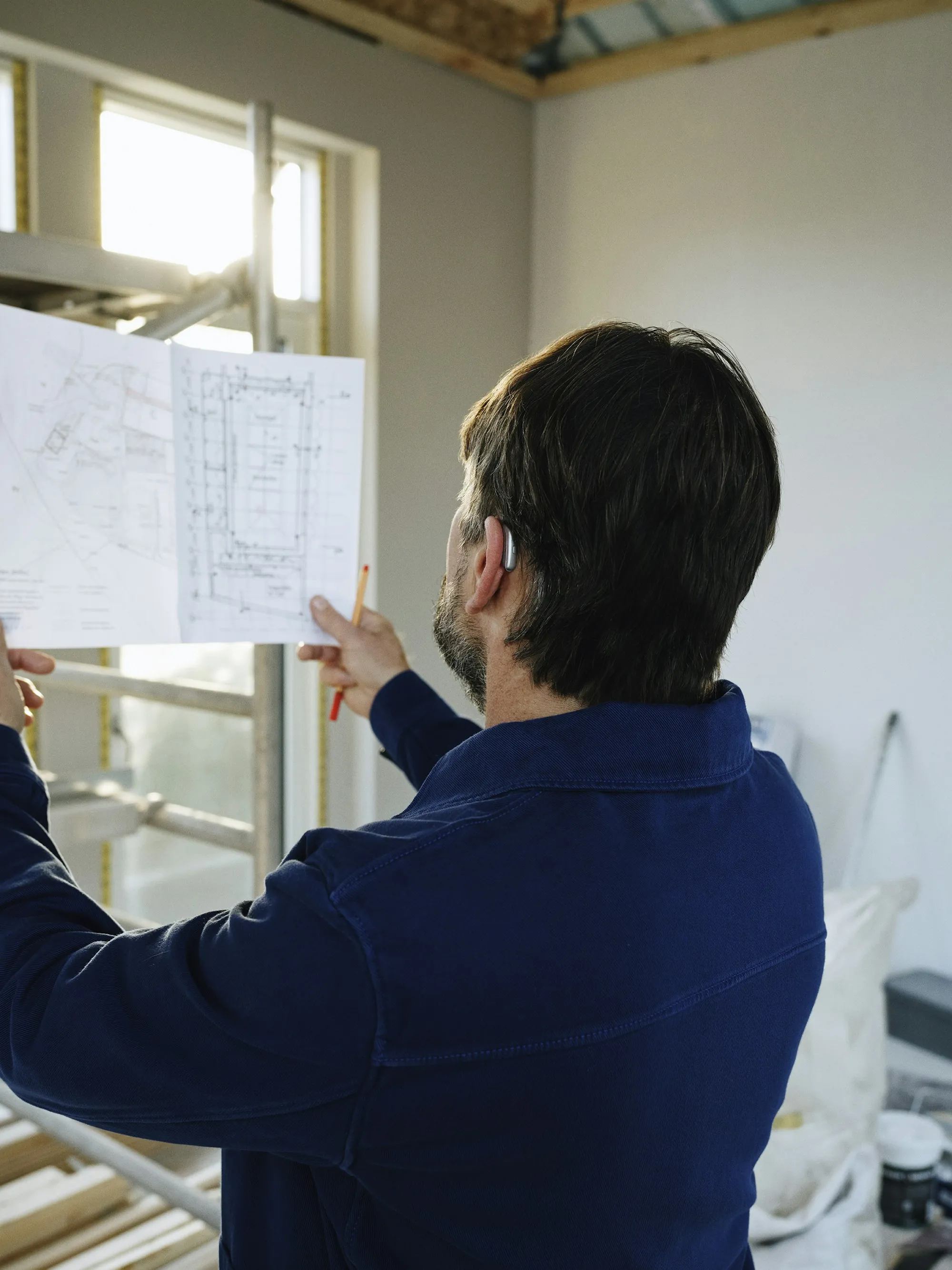 Contractor reviewing printed floor plans inside a home under renovation