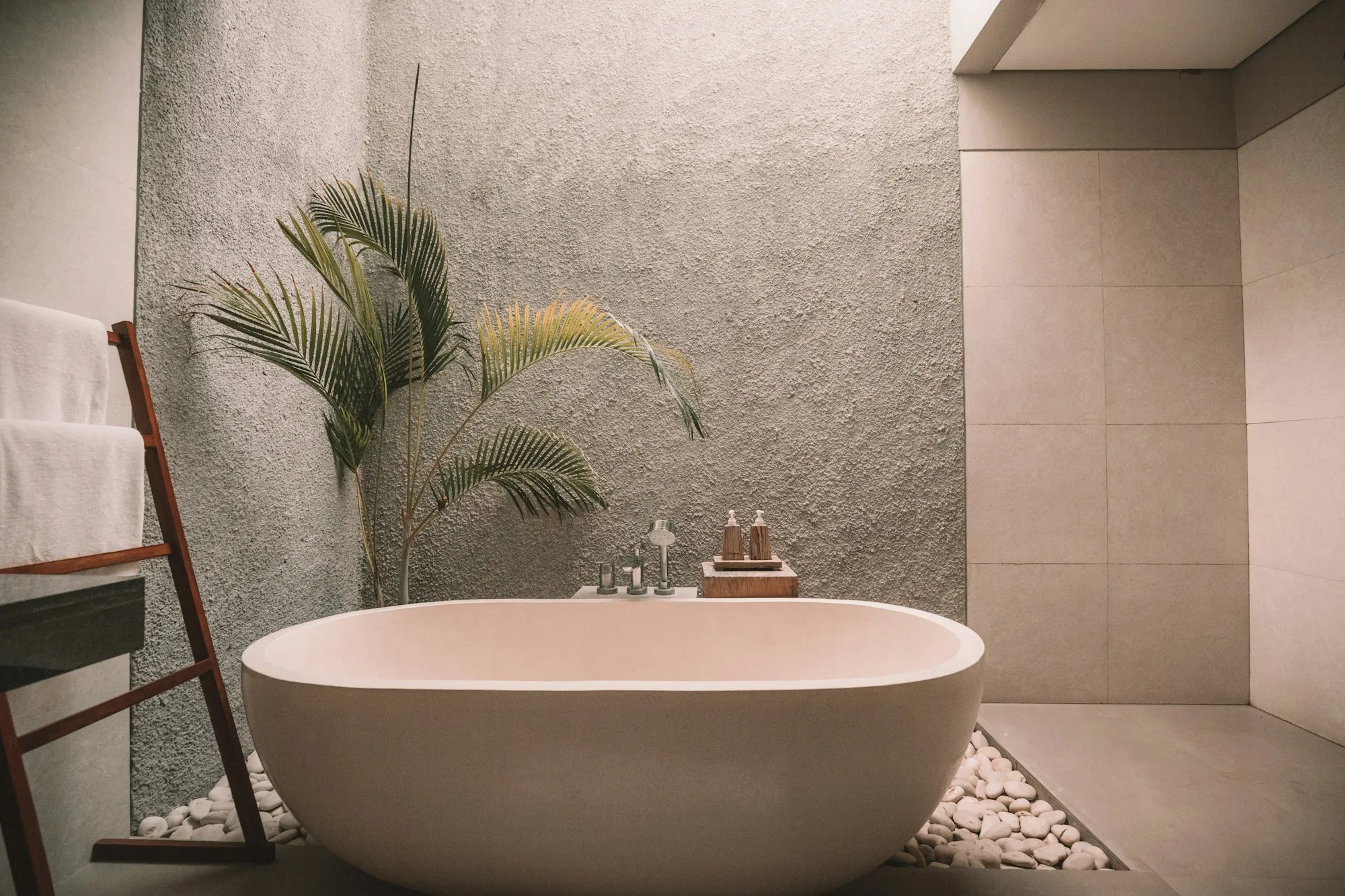 Freestanding soaking tub beside a potted palm in a plaster-walled bathroom