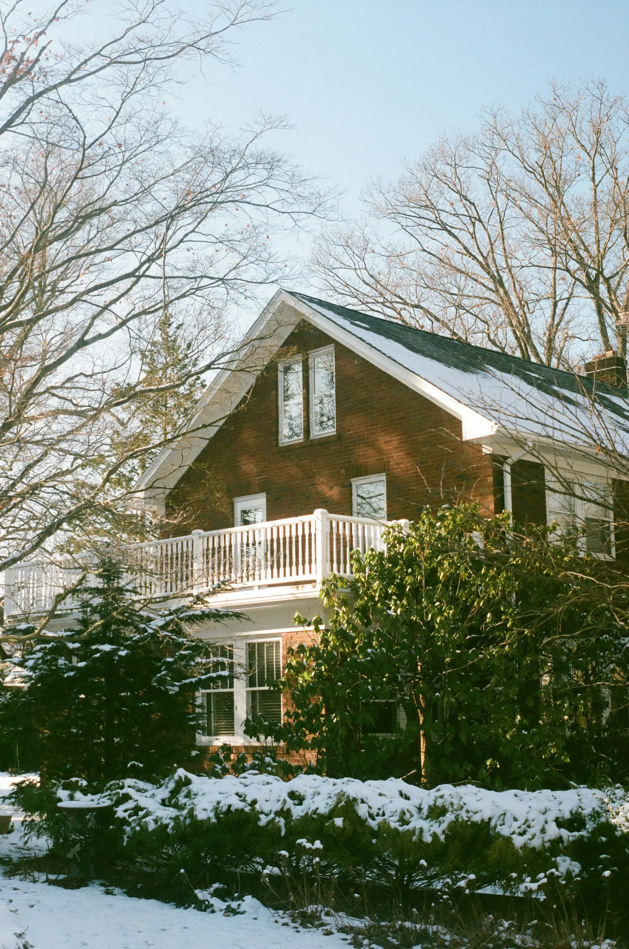 Brick home with a second-floor balcony behind snow-covered shrubs