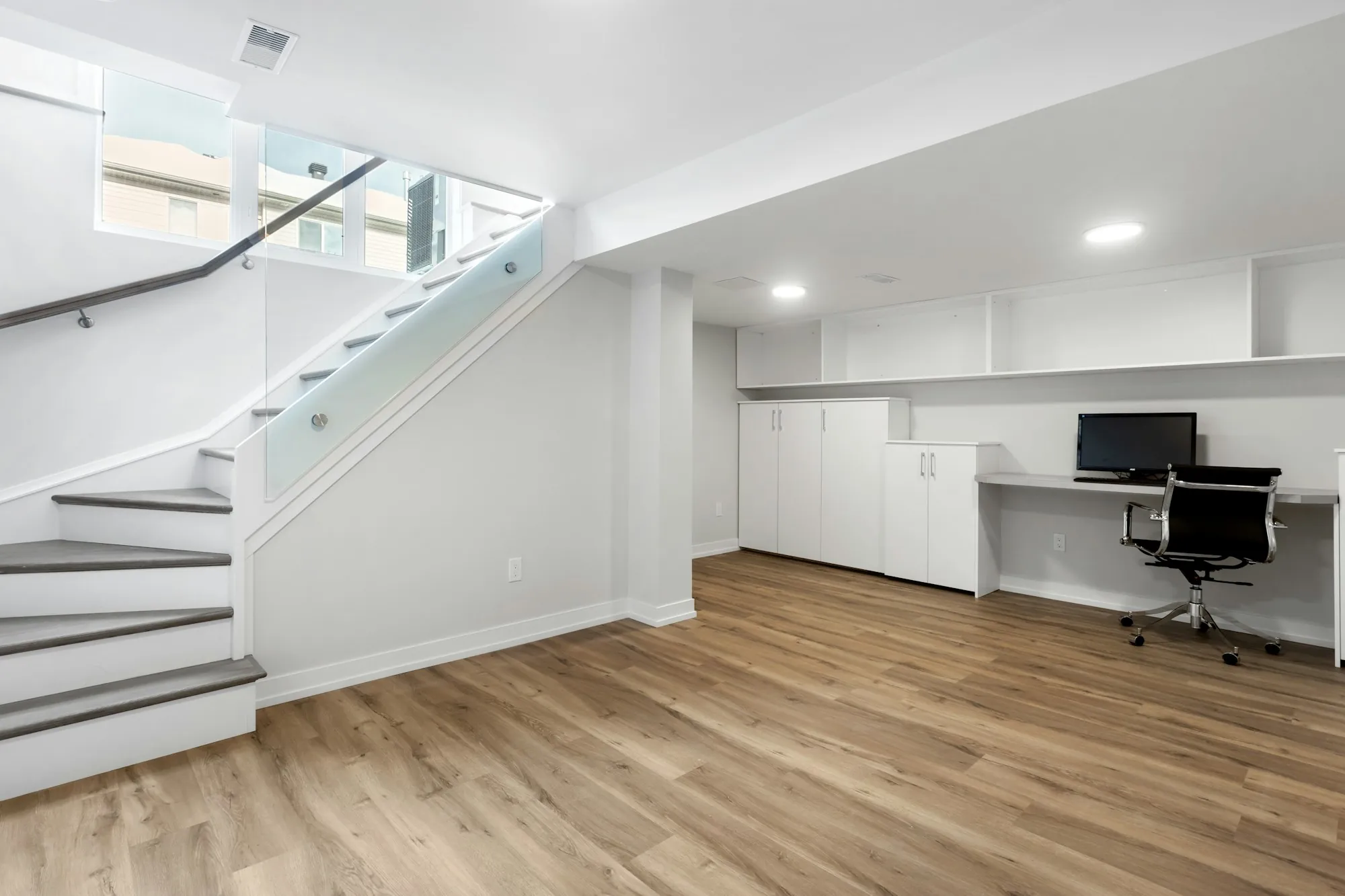 Finished lower level with a glass-railed staircase, built-in desk and wood-look flooring