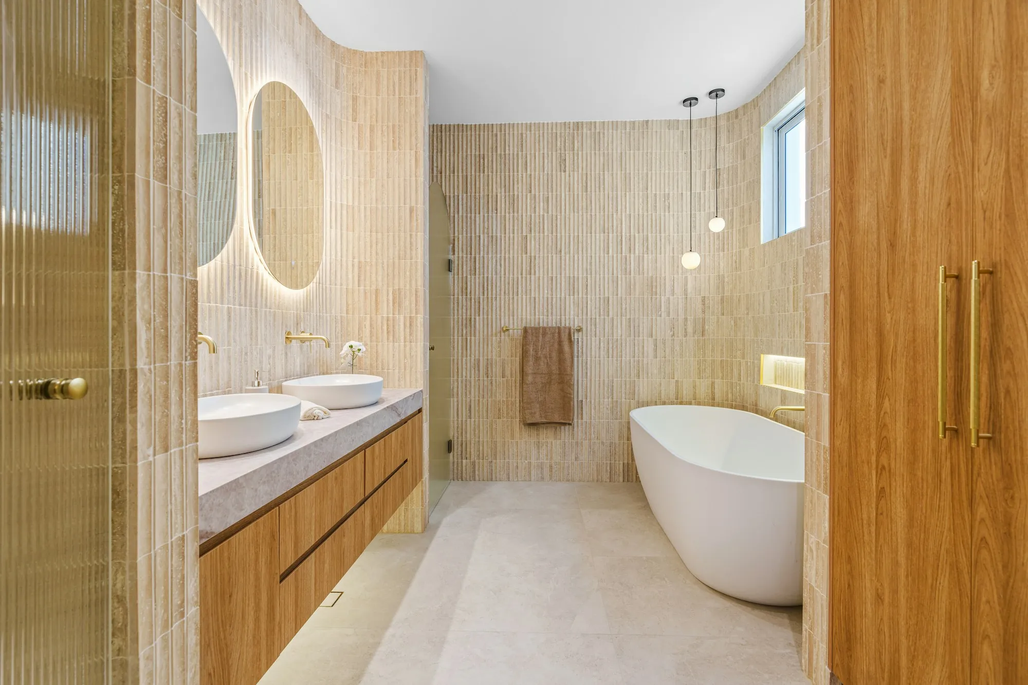 Bathroom with double vessel sinks, a freestanding tub and warm vertical tile